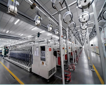 Spinning hall at RyderTex: rows of spinning frames in one-point perspective, bobbins of white yarn on every station.